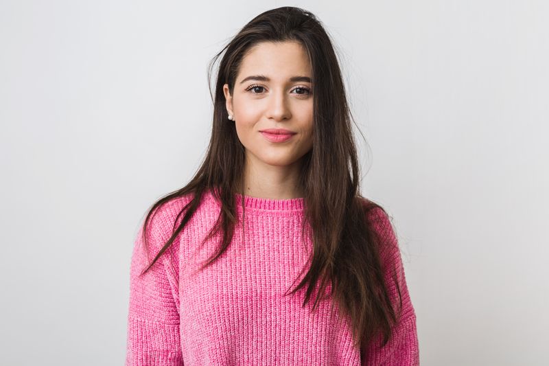 young and beautiful woman in pink warm sweater, natural look, smiling, portrait on white studio background, isolated, long hair